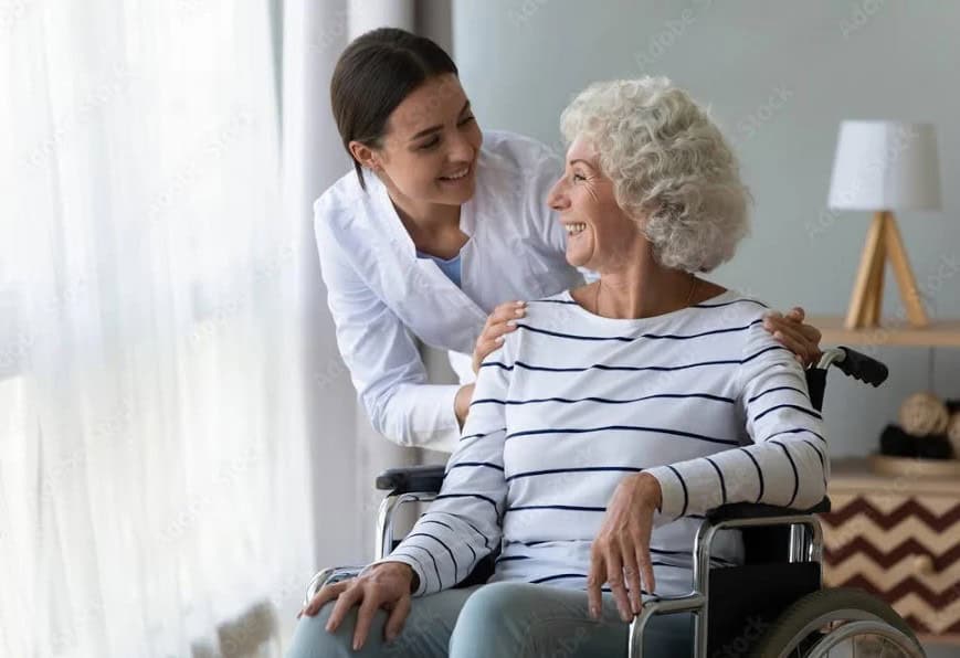 Elderly woman in wheelchair smiling with caregiver at home.