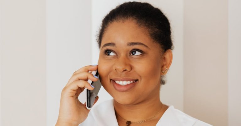 Smiling woman in white top using smartphone indoors with striped background.